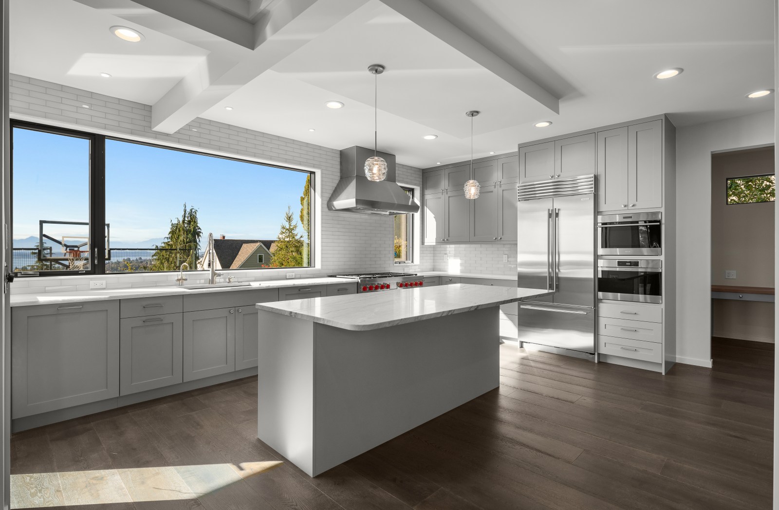 Soft gray shaker custom kitchen cabinets with professional appliances, stone island and water view