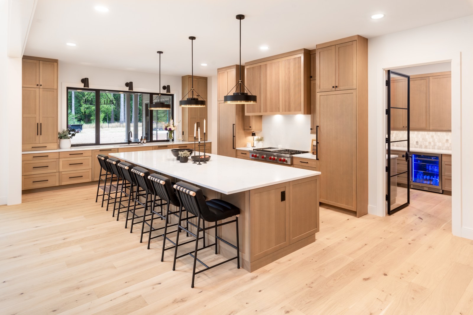 Warm oak shaker kitchen cabinets with an oversized white stone island and adjacent beverage room