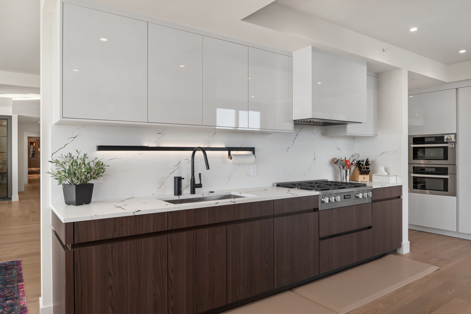 Modern walnut lower kitchen cabinets with glossy white uppers, integrated black pulls and full-height stone backsplash