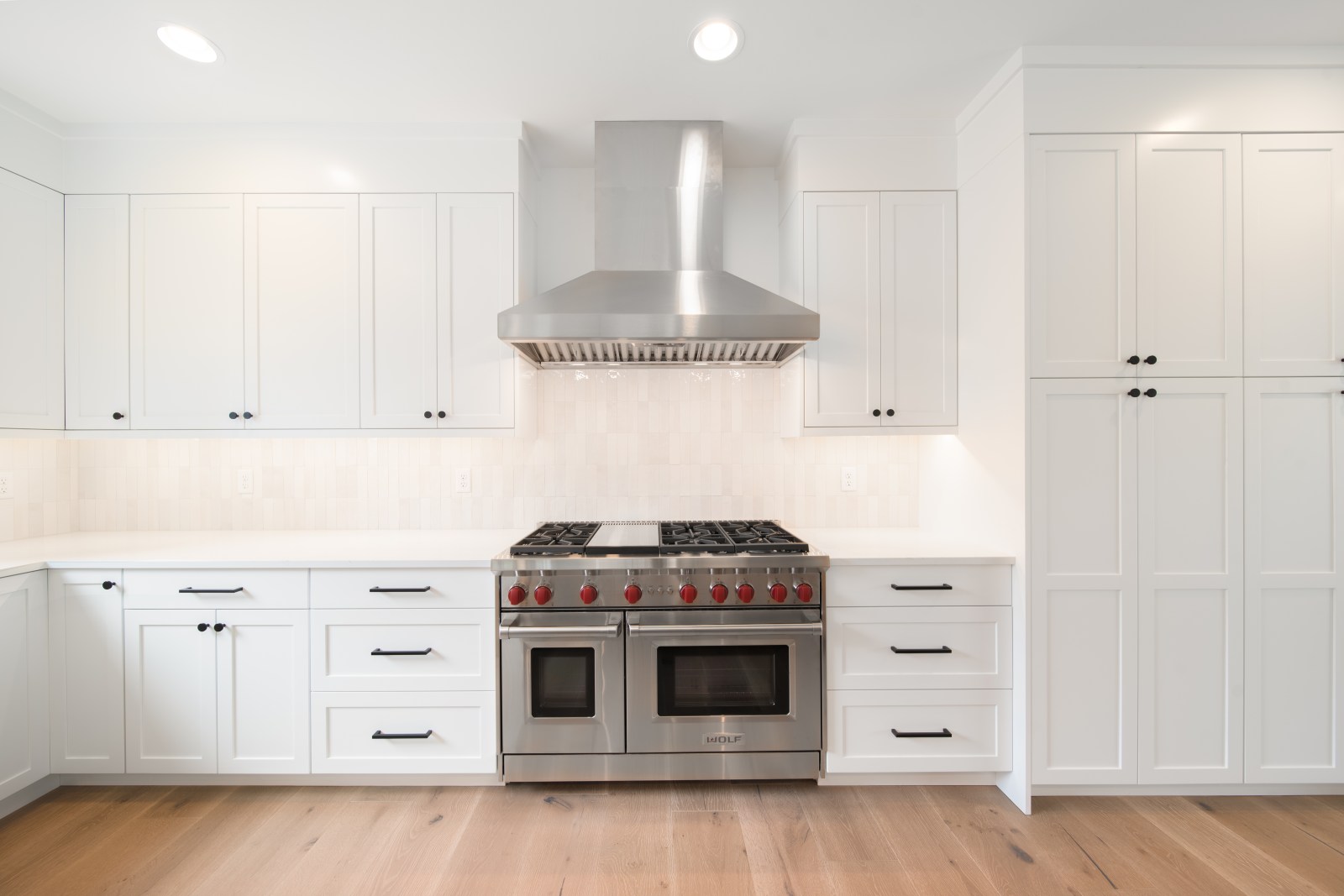 White shaker kitchen cabinetry surrounding a professional range with black hardware and tall pantry cabinets
