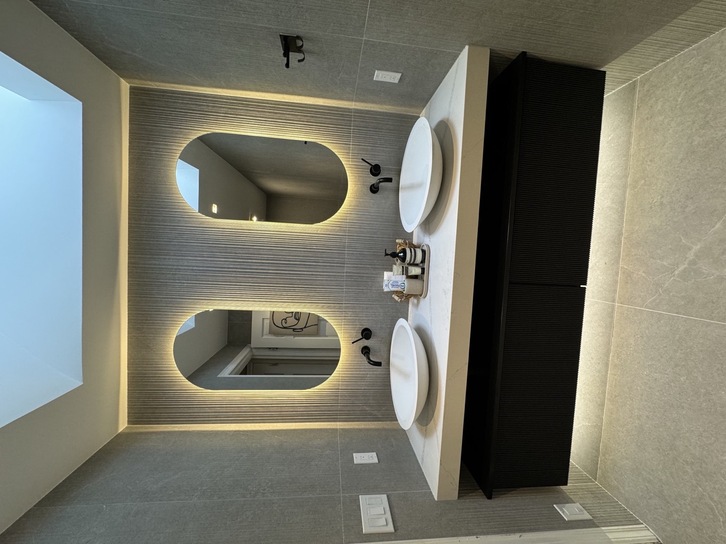 Textured gray tile, floating vanity and illuminated mirrors in a completed LeviArs bathroom