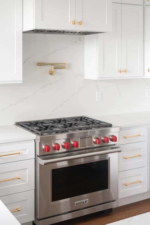 Stainless-steel gas range with red controls and brass pot filler