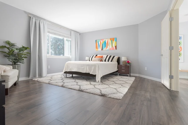 Bedroom with gray wood-look flooring, pale walls and a large window