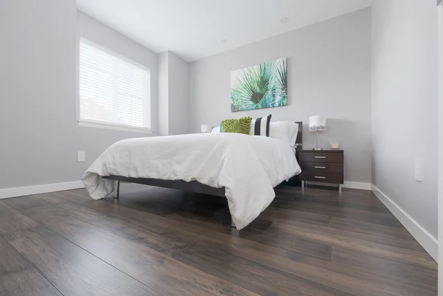Gray wood-look bedroom flooring beneath a white bed and dark nightstand
