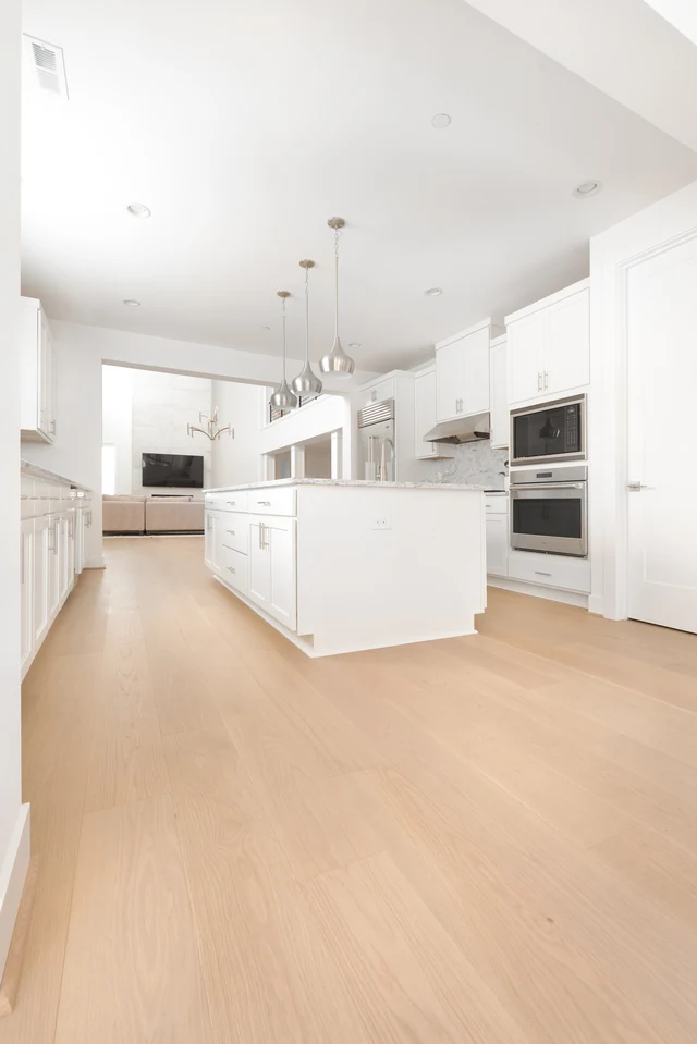 Open white kitchen with pale flooring and long island countertop