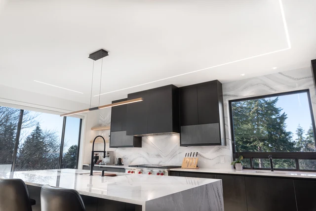 Kitchen sink island facing dark cabinets, range hood and trees