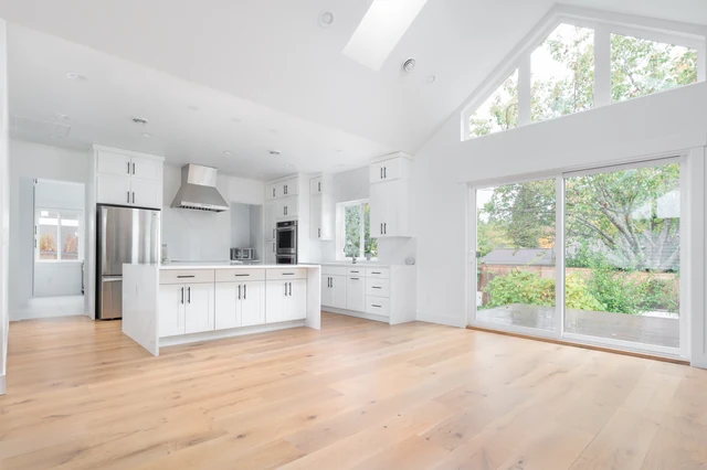 White kitchen and connected living area with wood flooring and a vaulted ceiling in a completed LeviArs multi-room project