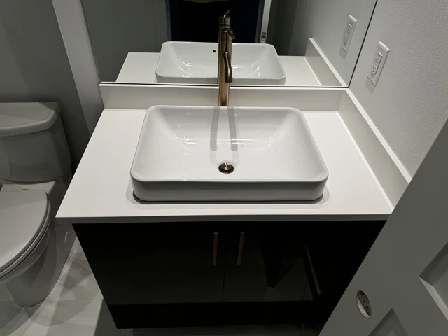 White vessel sink and brushed brass faucet installed on a dark bathroom vanity with quartz countertop