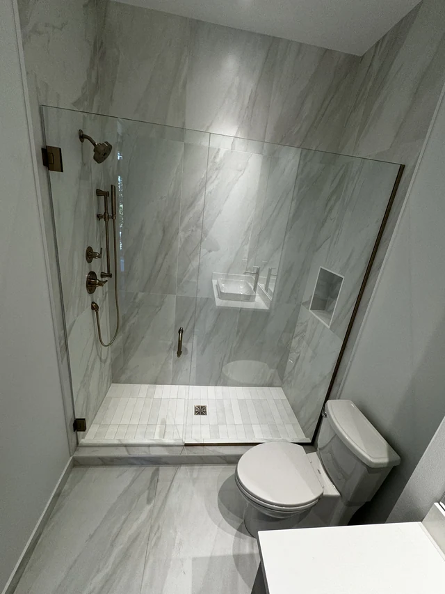 Walk-in shower finished with large-format marble-look porcelain tile, recessed niche and frameless glass
