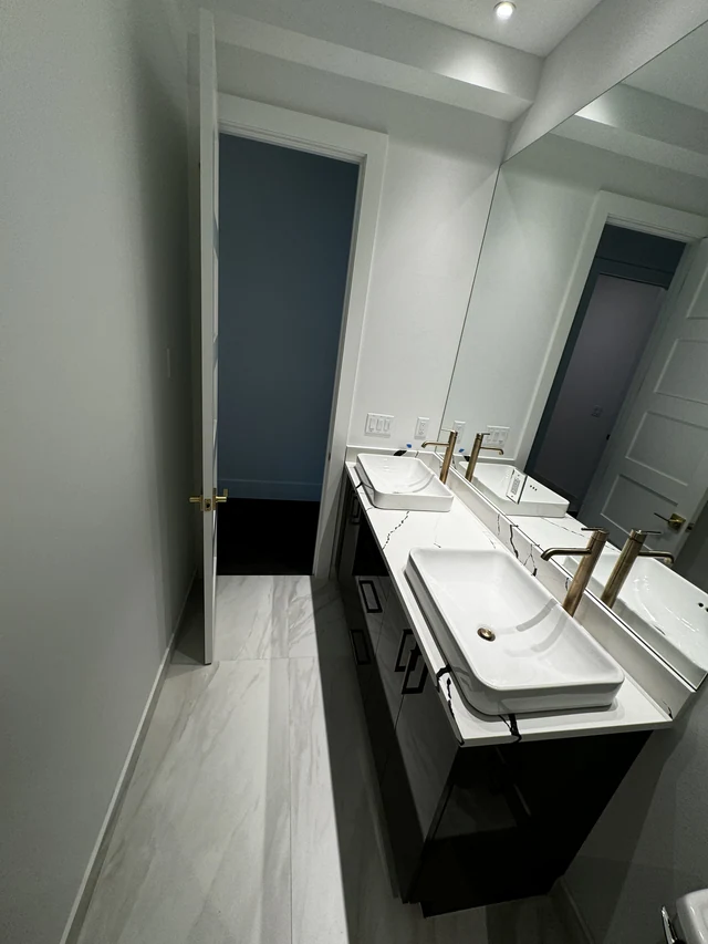Floating-style dark double vanity with vessel sinks, mirrored wall and integrated bathroom lighting
