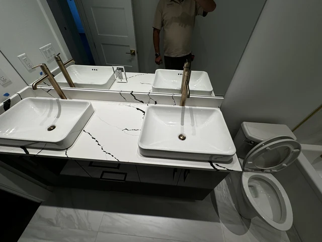 Close view of two white vessel sinks, brass faucets and dramatic veined bathroom countertop
