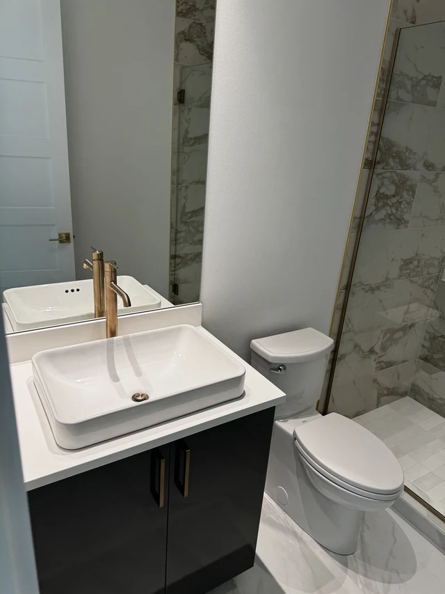 Vessel sink with brass faucet beside a coordinated marble-look porcelain shower wall