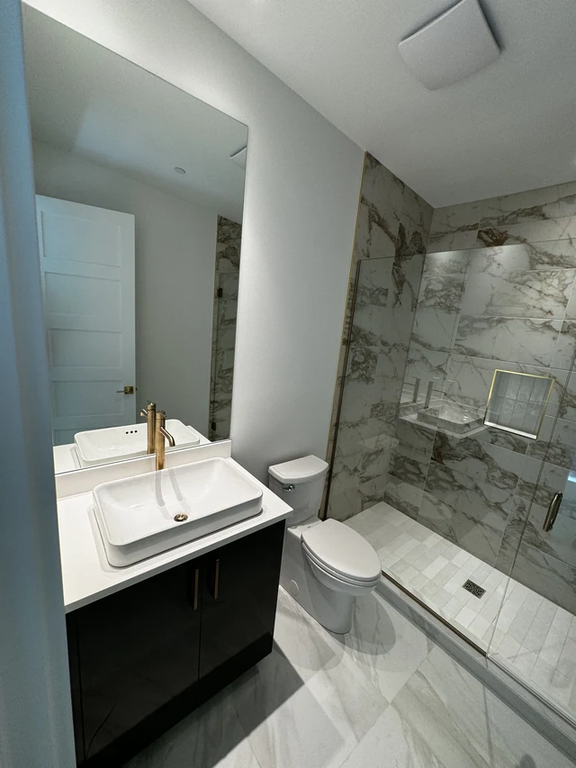 Compact bathroom remodel with dark vanity, vessel sink, toilet and glass-enclosed porcelain shower