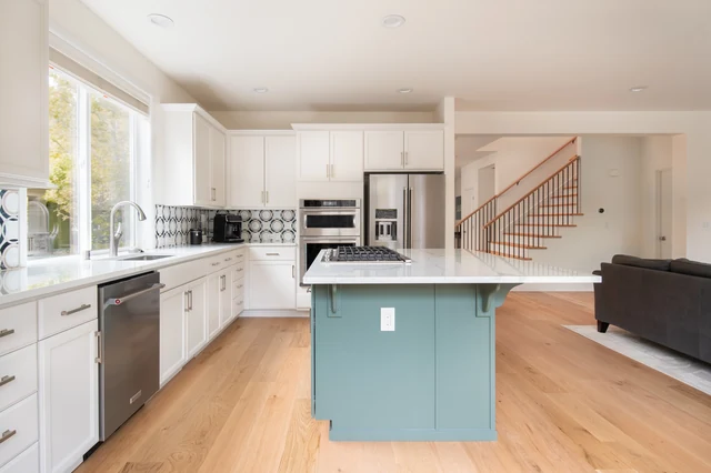 Green kitchen island with gas cooktop, white cabinets and stainless-steel appliances