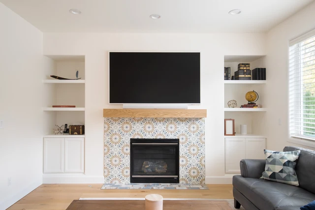 Patterned tile fireplace with wood mantel, television and white built-in shelving