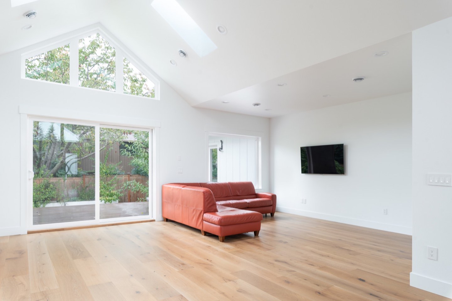 Vaulted living area with large windows, wood flooring and a red sofa in the same Branislav home