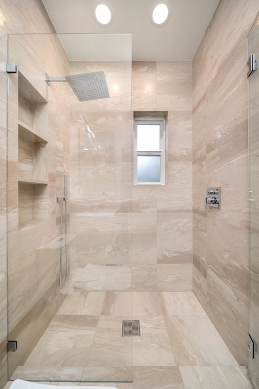 Glass-enclosed shower with stone-look tile and square drain