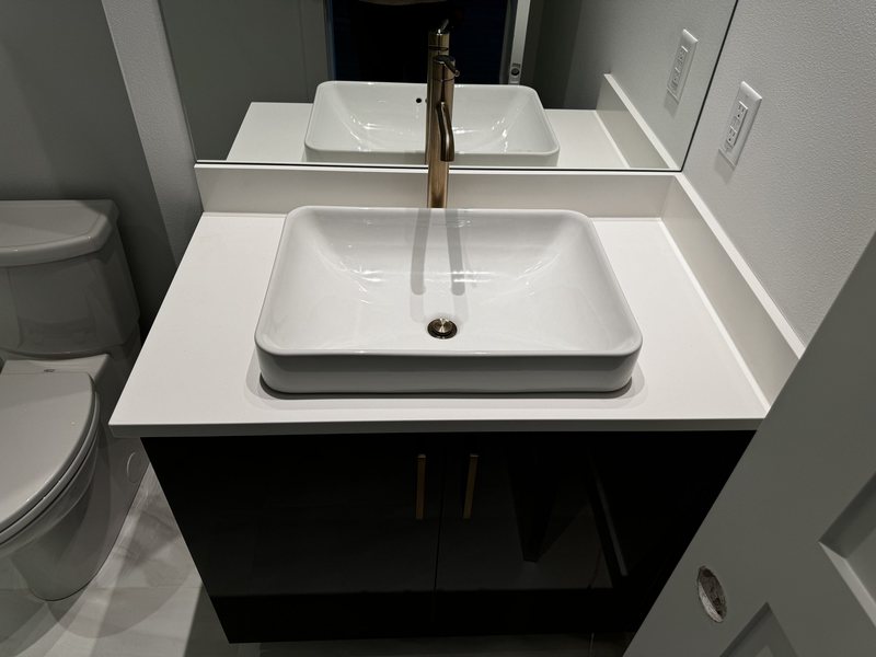 White vessel sink and brushed brass faucet installed on a dark bathroom vanity with quartz countertop