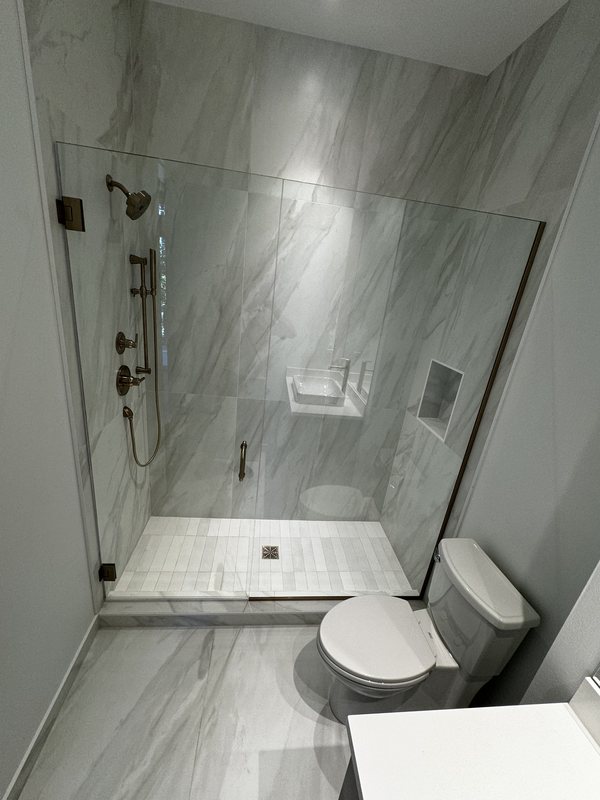 Walk-in shower finished with large-format marble-look porcelain tile, recessed niche and frameless glass