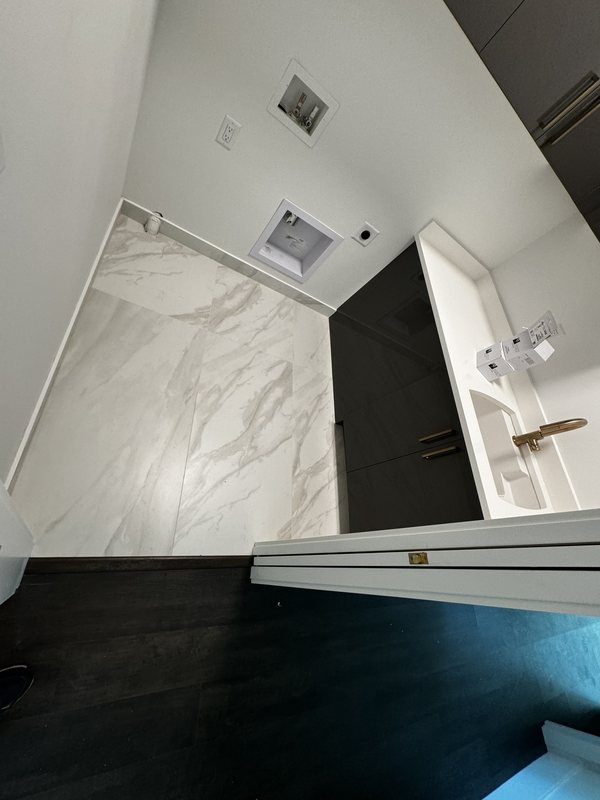 Primary bathroom entrance with light porcelain floor tile and a long dark double vanity