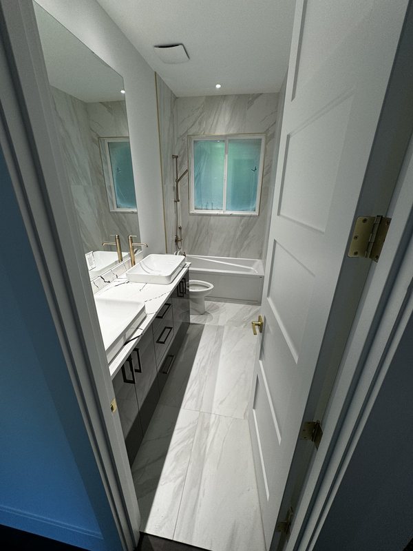 Long primary bathroom layout with dual sinks, porcelain flooring and a freestanding tub below the window
