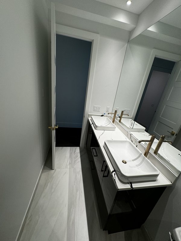 Floating-style dark double vanity with vessel sinks, mirrored wall and integrated bathroom lighting
