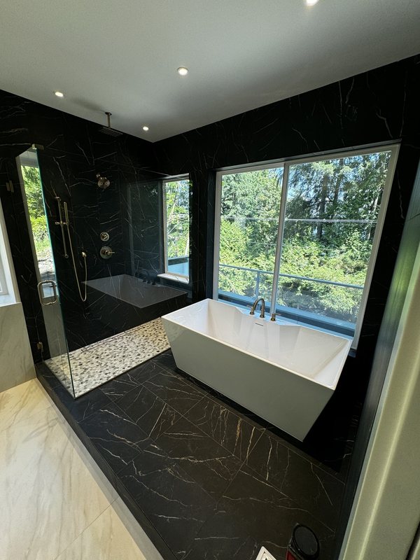 Black porcelain primary bathroom with a freestanding white tub and expansive garden windows