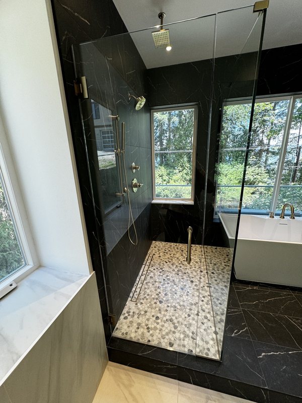 Walk-in shower with black large-format porcelain tile, pebble mosaic floor and brass shower fixtures