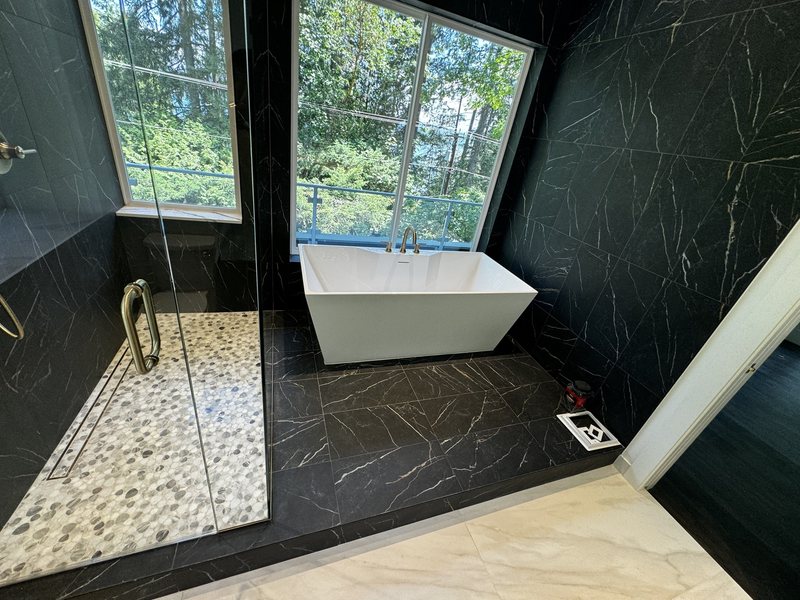 Freestanding tub beside a black porcelain shower with pebble mosaic floor and floor-to-ceiling glass