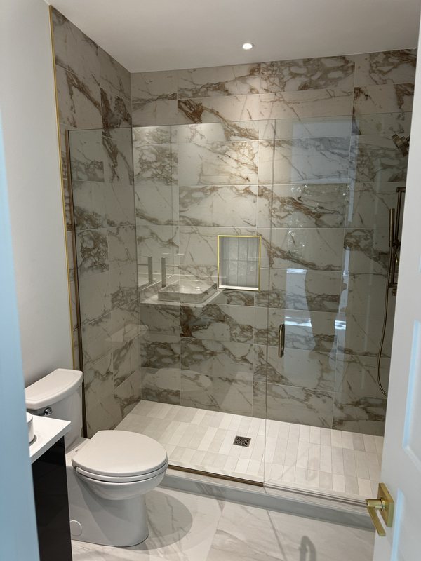 Bathroom shower finished with richly veined porcelain tile, frameless glass and brushed brass trim