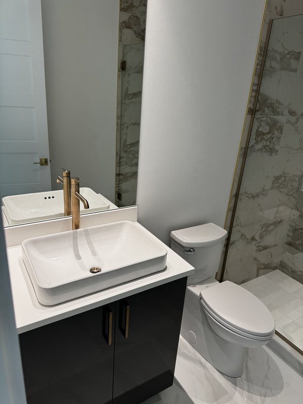 Vessel sink with brass faucet beside a coordinated marble-look porcelain shower wall