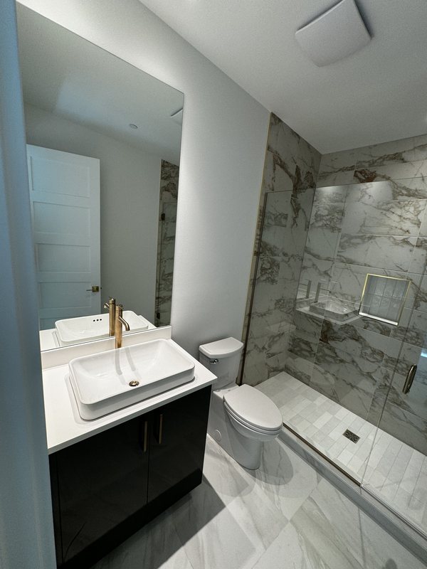 Compact bathroom remodel with dark vanity, vessel sink, toilet and glass-enclosed porcelain shower