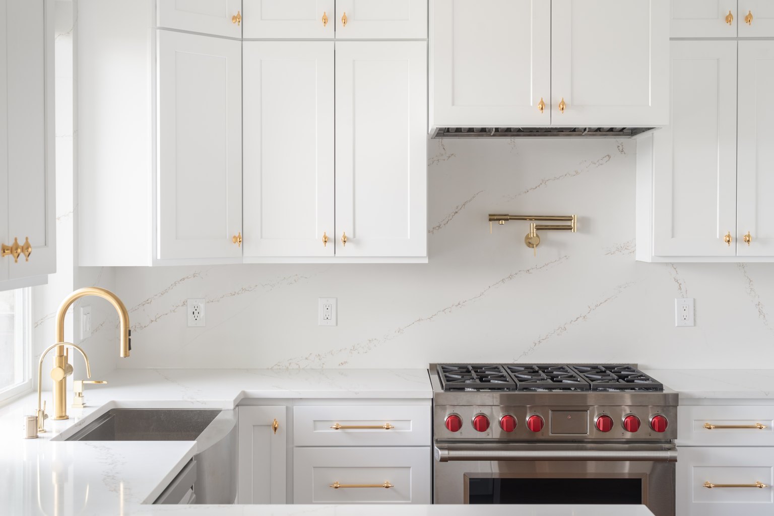 White kitchen cabinetry with warm brass handles and a brass faucet