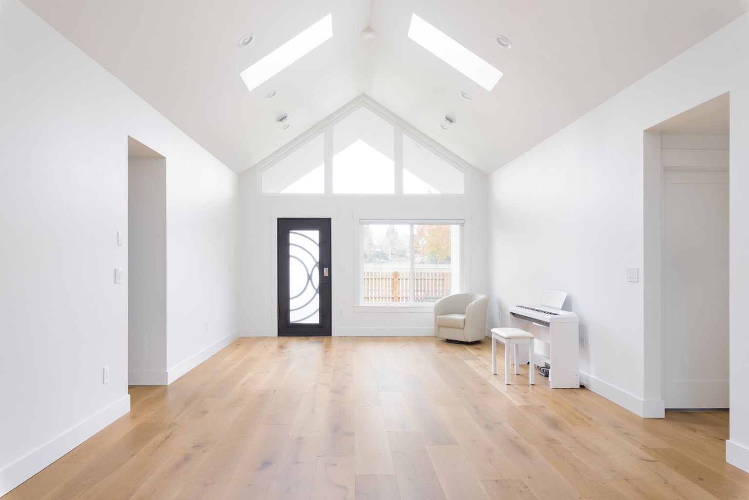 White walls, vaulted ceiling and trim in a living room with light wood flooring