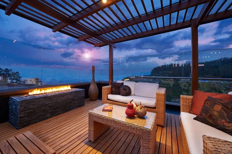 Covered wood deck with woven lounge seating, a coffee table and linear fire feature at dusk