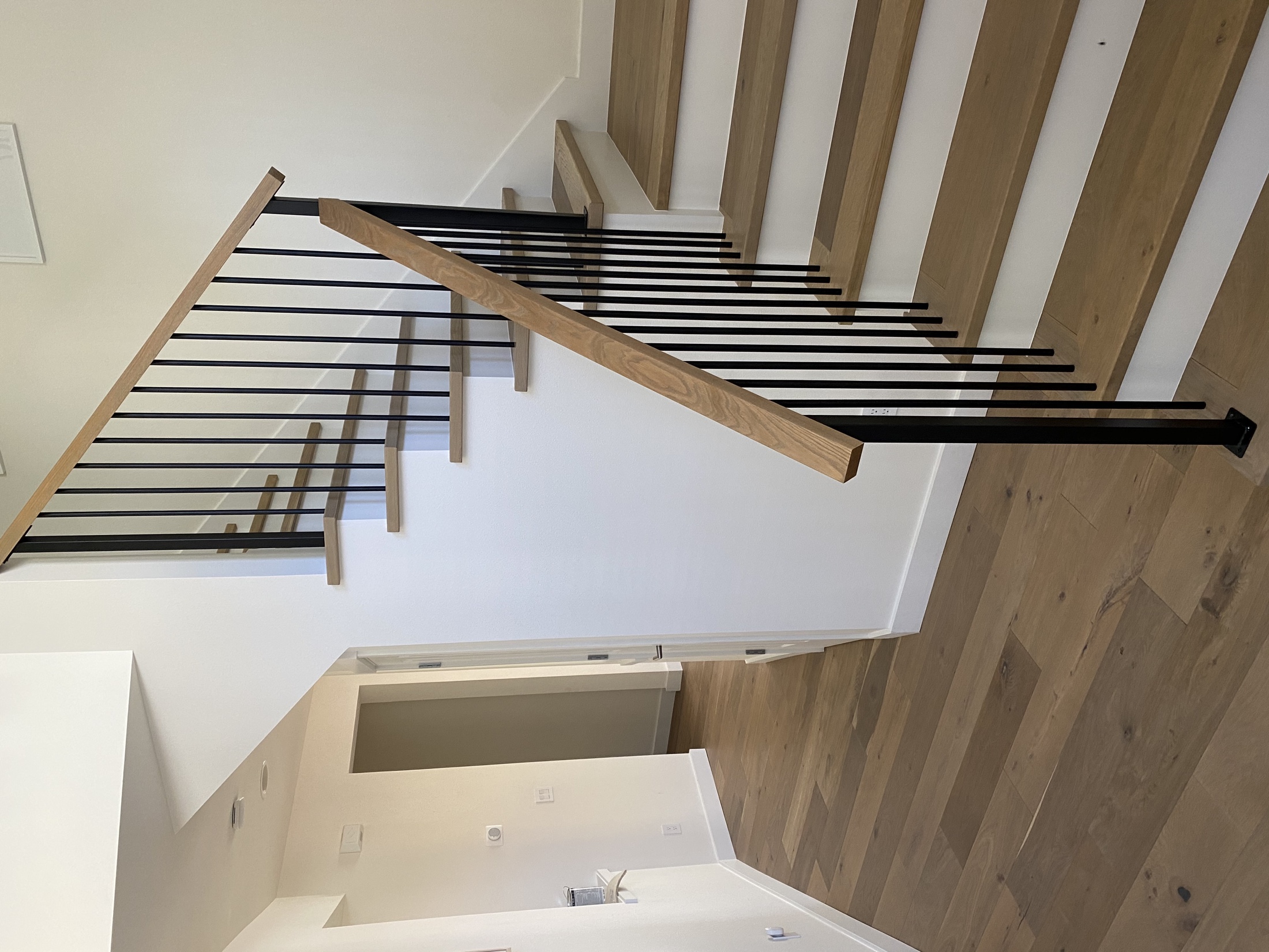 Contemporary staircase with light wood treads, white risers, slim dark balusters and a wood handrail