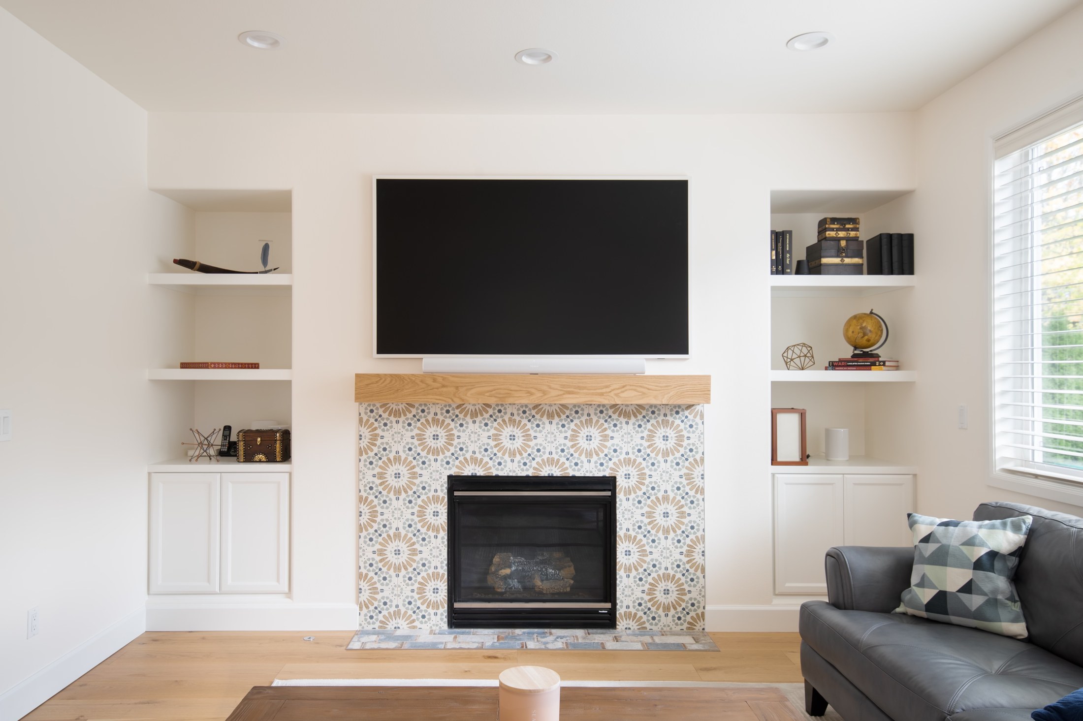 Patterned tile fireplace surround beneath a wood mantel between white built-in shelves