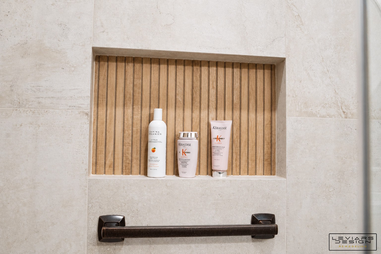 Recessed shower niche with warm vertical textured backing, pale tile edges and a dark grab bar below