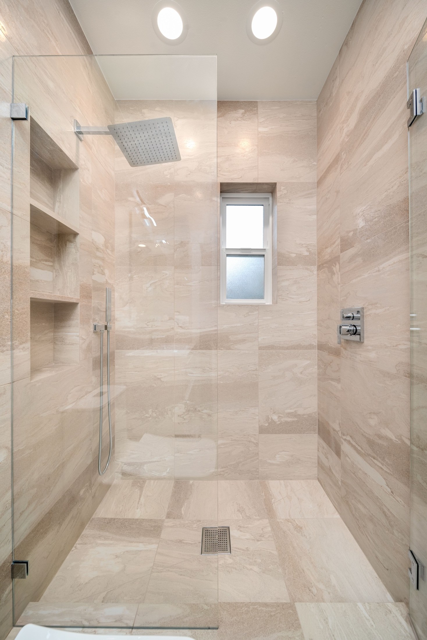 Completed shower with warm veined tile, three recessed niches, glass enclosure and a square floor drain