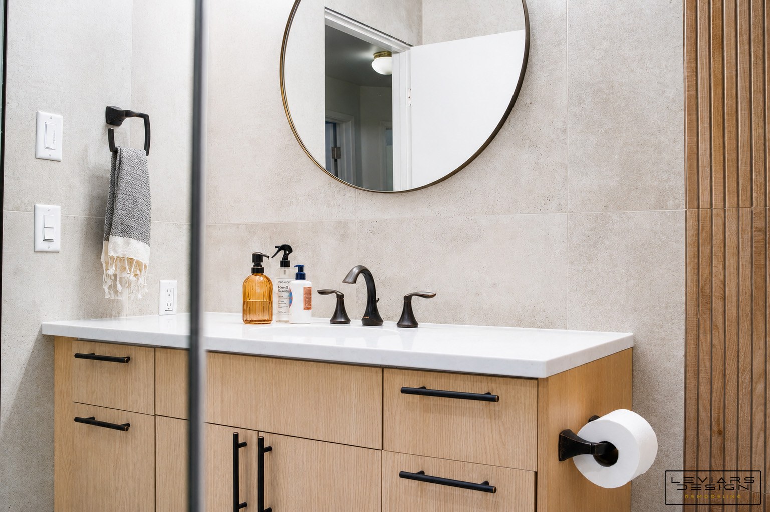 Pale tile behind a light wood bathroom vanity beside a warm vertically textured shower accent